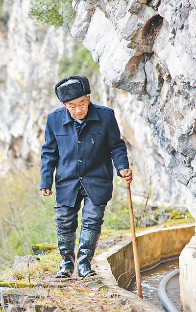 在水渠惊险处，黄大发低头侧身通过，身旁就是悬崖。.jpg