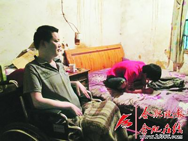 陈明元坐在轮椅上看着儿子子龙在床上做作业.jpg