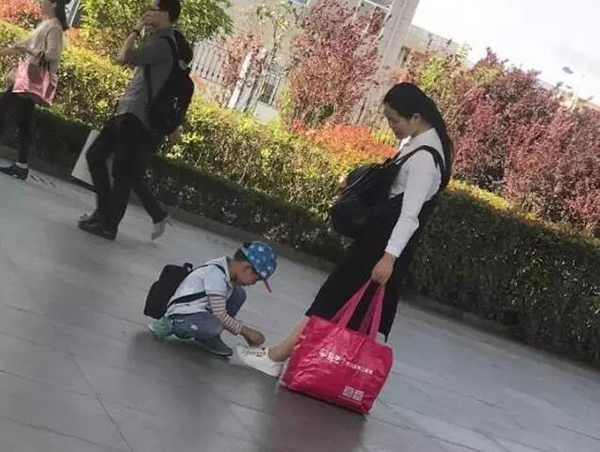 02：街边，小男孩为手提重物的妈妈细心系鞋带。他说：“虽然我不能帮妈妈分担重量，但我可以帮妈妈系鞋带保证她不会摔倒！”.jpg