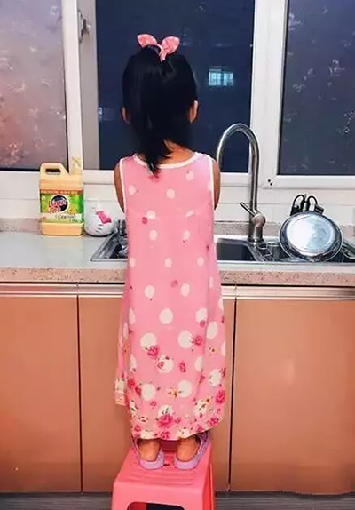 05：晚饭后，还没有洗碗台高小姑娘，踩着板凳洗起了碗。她说：“妈妈常跟奶奶抢着洗碗，我是在跟妈妈学。”.jpg